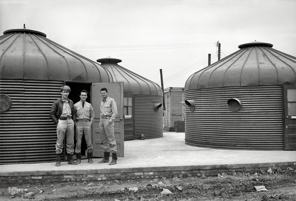 The meme is a black-and-white image of three men in military uniforms standing in front of a row of bunkers or shelters. The image is captioned "When you're trying to get out of work but your boss is always on your case"